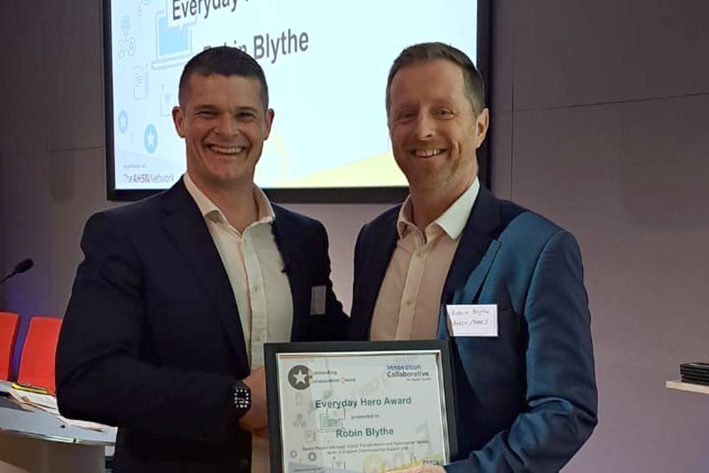 Two men smiling, both holding a presented certificate