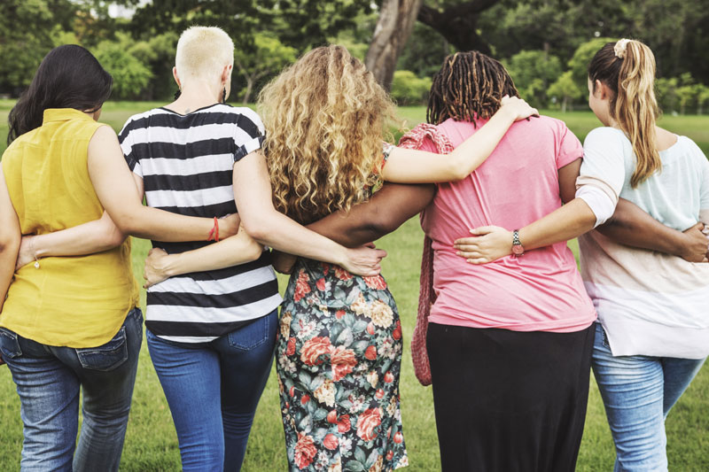 Five women walking arm in arm away from camera