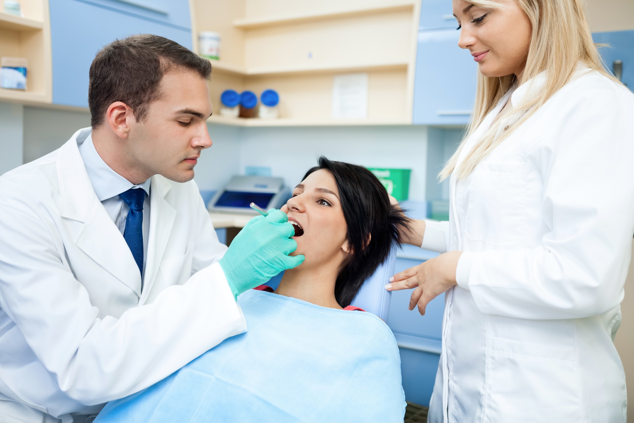 Male dentist performing dentistry on female patient observed by female colleague