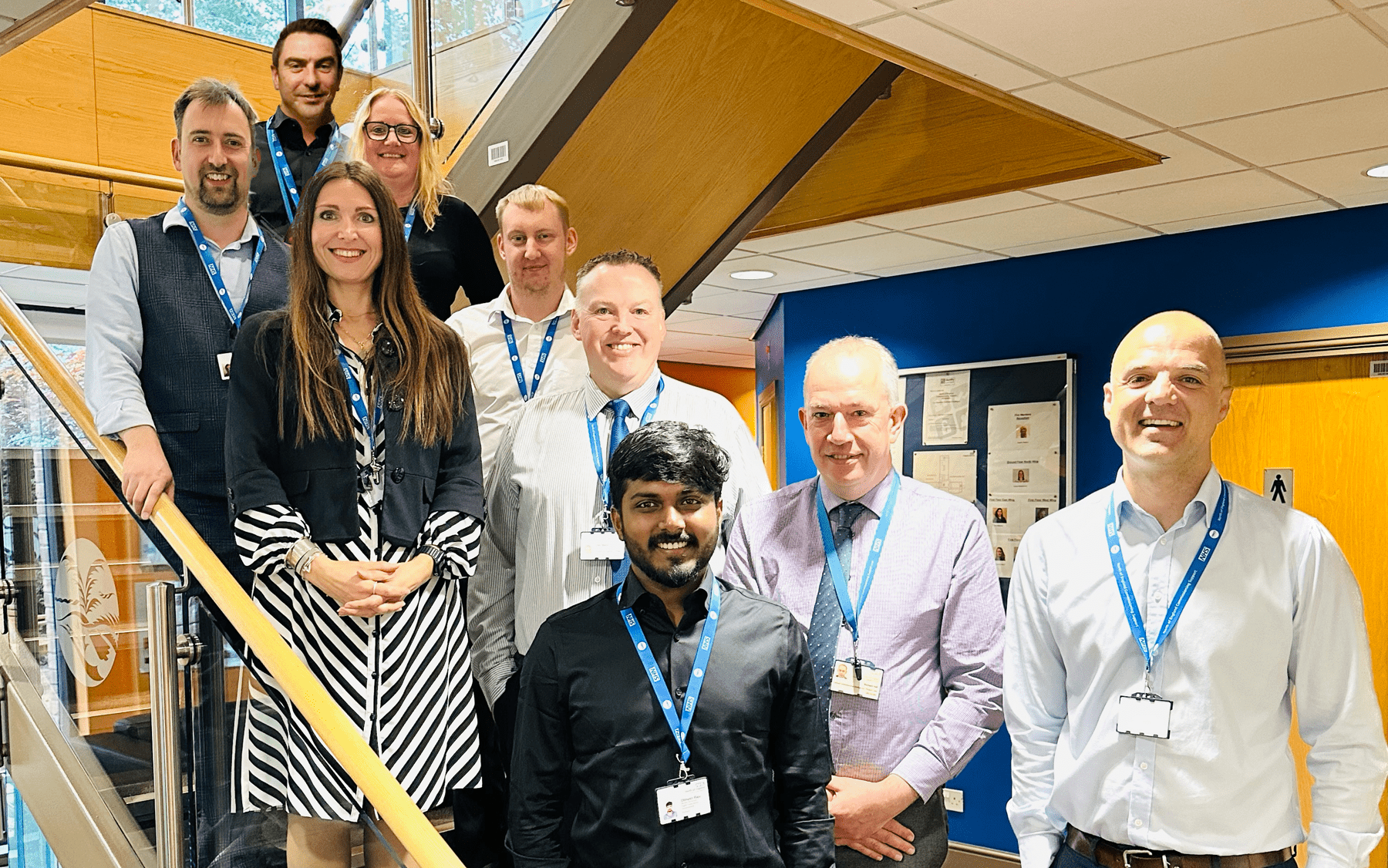 NECS' UEC RAIDR SCC app team standing for a team photo, arranged around a staircase