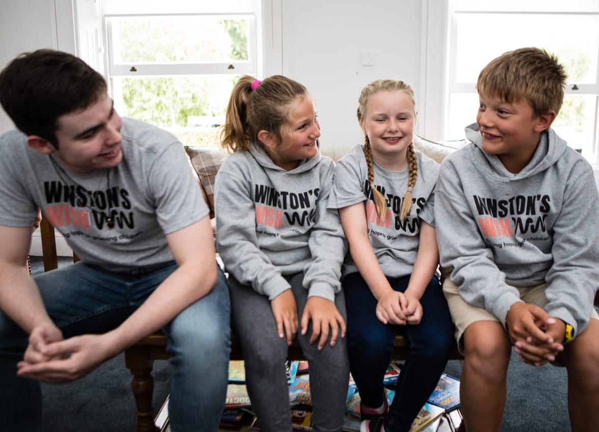 Two girls and two boys sat smiling at each other wearing Winston's Wish hoodies and t-shirts