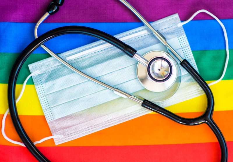 LGBT flag with a face mask and stethoscope laid on top of it