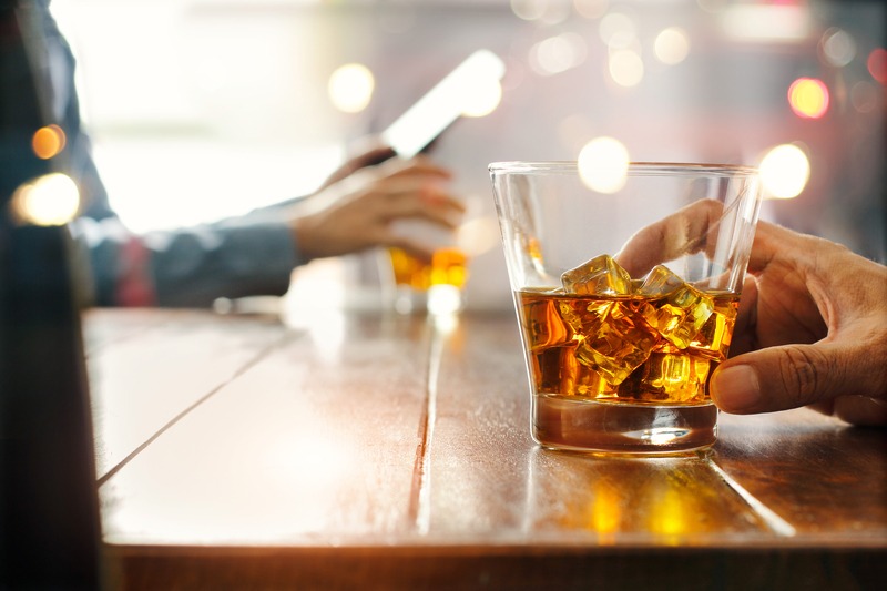 Hand touching a glass with whisky and ice, on a bar