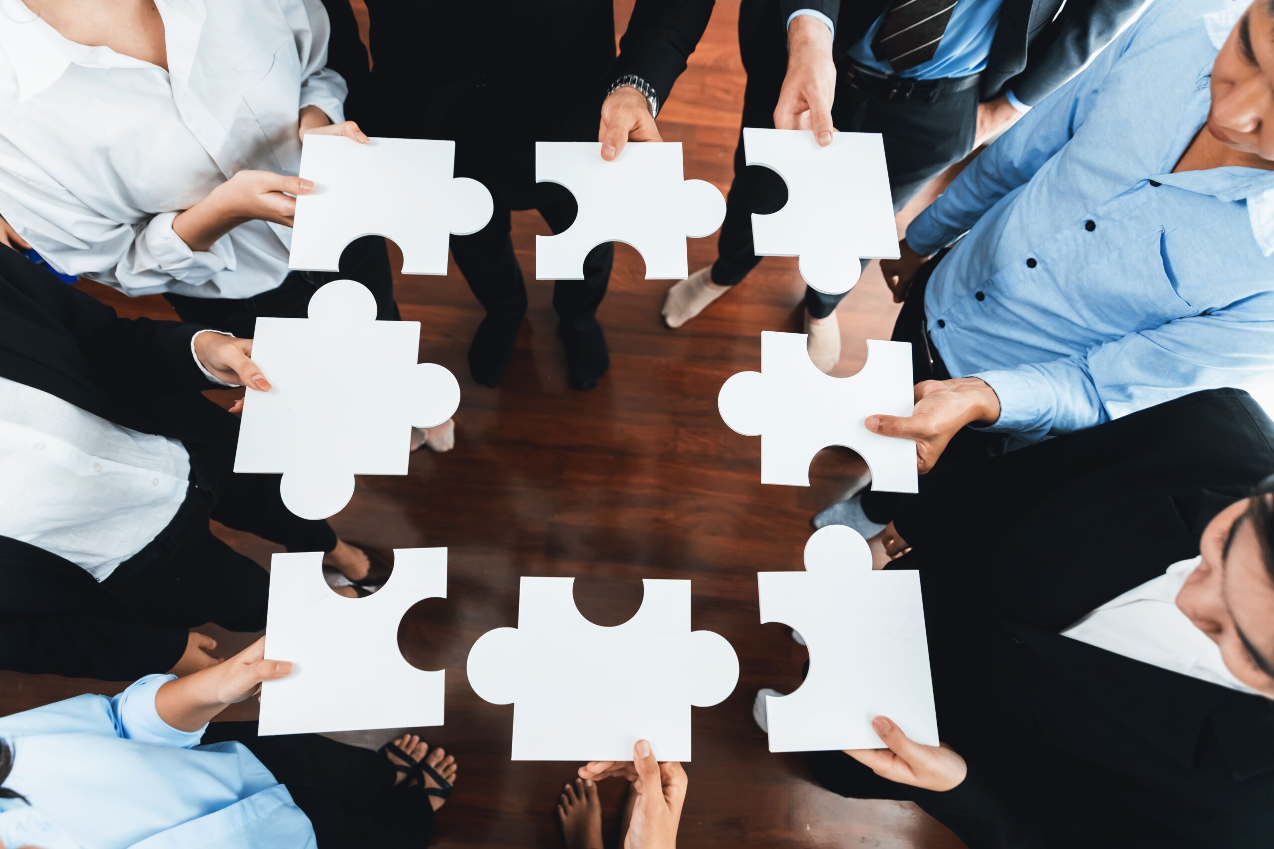shutterstock_2237569391 A group of people standing in a square holding pieces of white jigsaw trying to fit them together