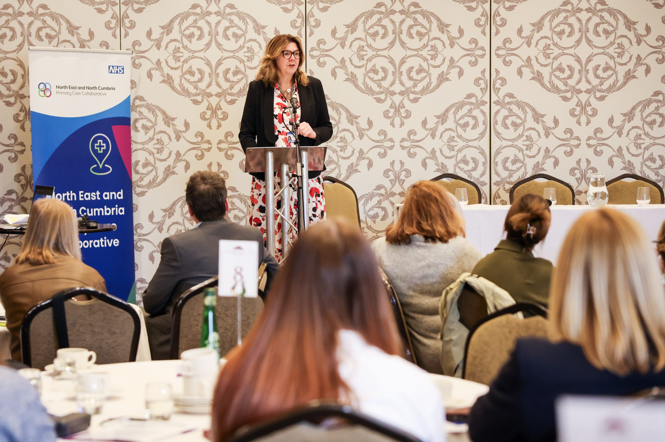 Claire Fuller standing at a lectern speaking in front of delegates