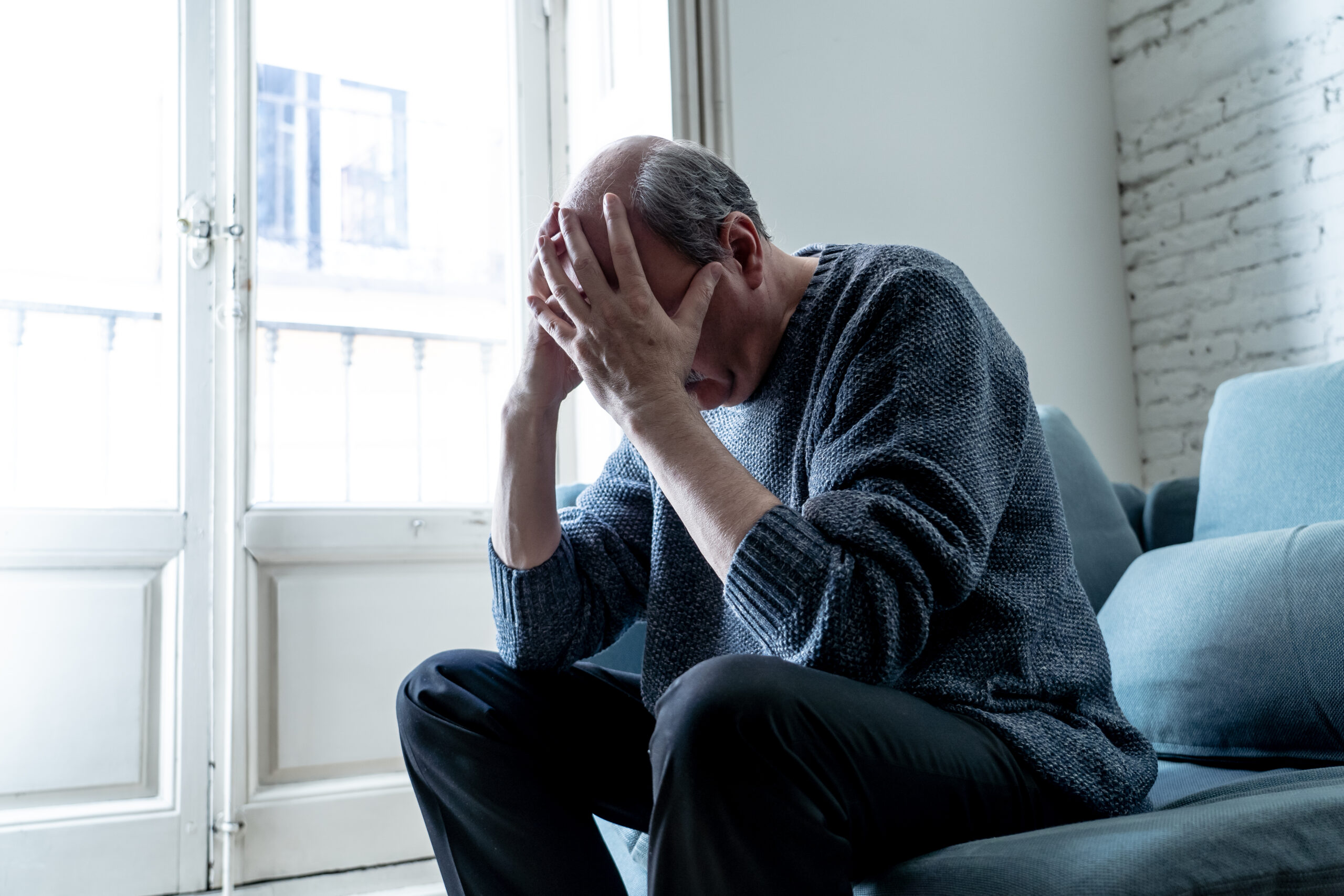 Overwhelmed old senior man suffering alone at home feeling confused sad alone on couch at home